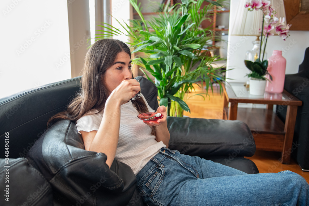 Young woman sitting on sofa at home enjoying cup of coffee Young woman sitting on sofa at home enjoying cup of coffee