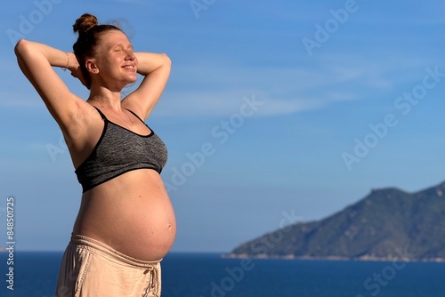 Young pregnant woman stroking her belly outdoors on sea, beach at summer vacation 