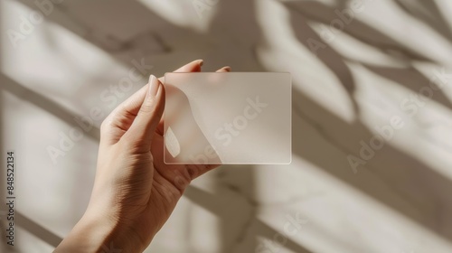 Minimalist Close-Up of Hand Holding Transparent Glass Card in Soft Sunlight