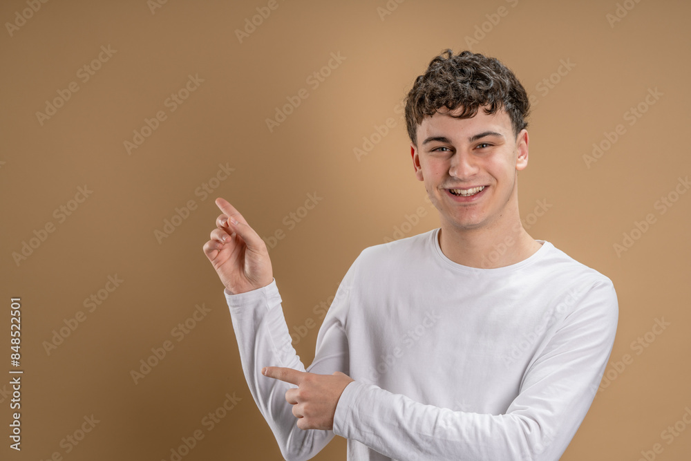 Portrait of one caucasian man 20 years old looking to the camera in front of almond color studio background smiling wearing casual shirt point on copy space Portrait of one caucasian man 20 years old looking to the camera in front of almond color studio background smiling wearing casual shirt point on copy space