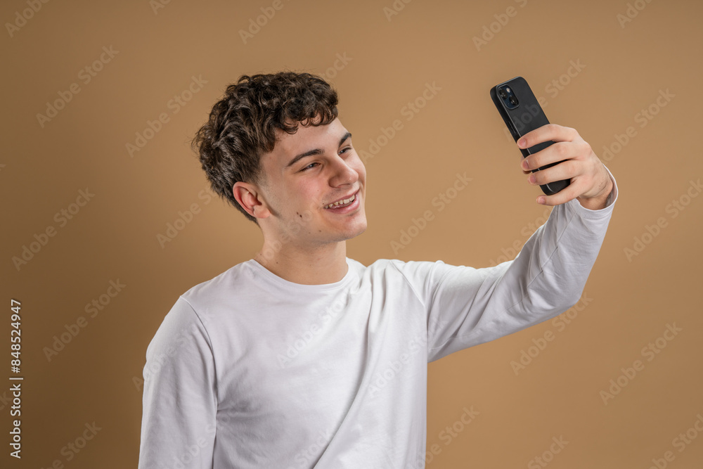 One man adult caucasian male teenager stand studio shot happy smile use mobile phone smartphone to make a call talking video call or self portrait selfie copy space in front of beige background One man adult caucasian male teenager stand studio shot happy smile use mobile phone smartphone to make a call talking video call or self portrait selfie copy space in front of beige background