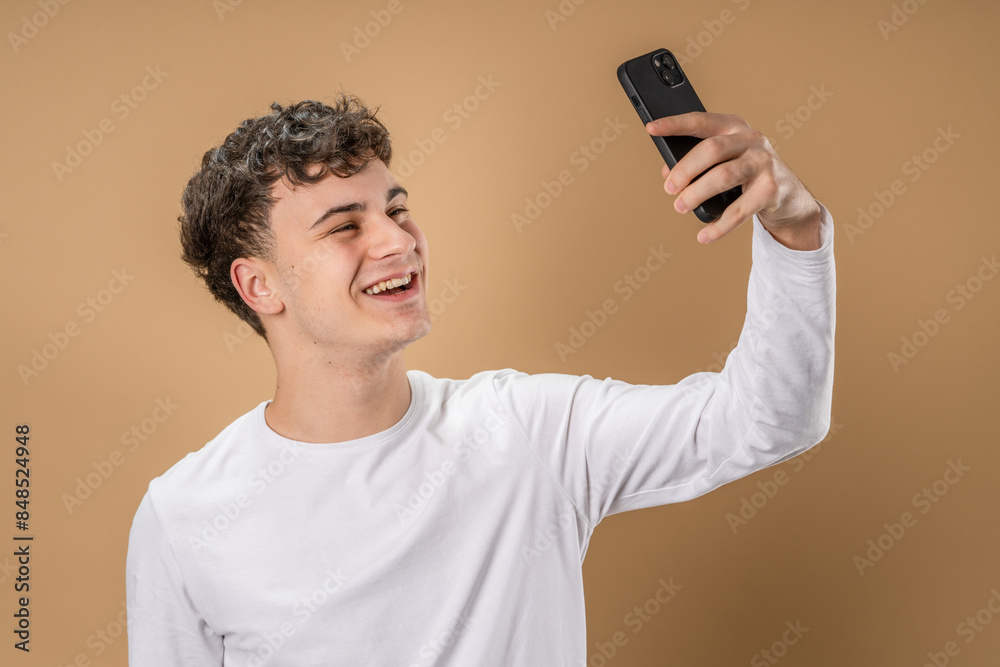 One man adult caucasian male teenager stand studio shot happy smile use mobile phone smartphone to make a call talking video call or self portrait selfie copy space in front of beige background One man adult caucasian male teenager stand studio shot happy smile use mobile phone smartphone to make a call talking video call or self portrait selfie copy space in front of beige background
