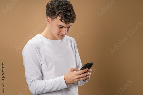 One man caucasian male teenager boy use smartphone mobile phone for online internet browsing social network or sms text messages studio shot beige background happy smile © Miljan Živković