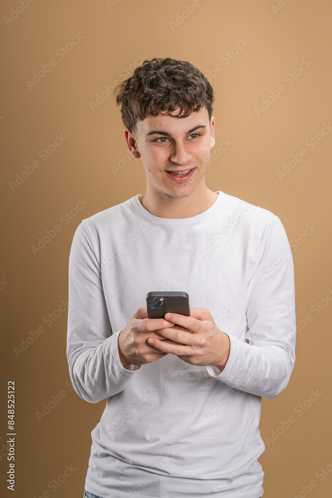 One man caucasian male teenager boy use smartphone mobile phone for online internet browsing social network or sms text messages studio shot beige background happy smile One man caucasian male teenager boy use smartphone mobile phone for online internet browsing social network or sms text messages studio shot beige background happy smile