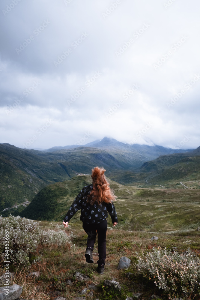 Eine Frau mit wehenden Haaren rennt kamera abgewand durch die Berge Eine Frau mit wehenden Haaren rennt kamera abgewand durch die Berge