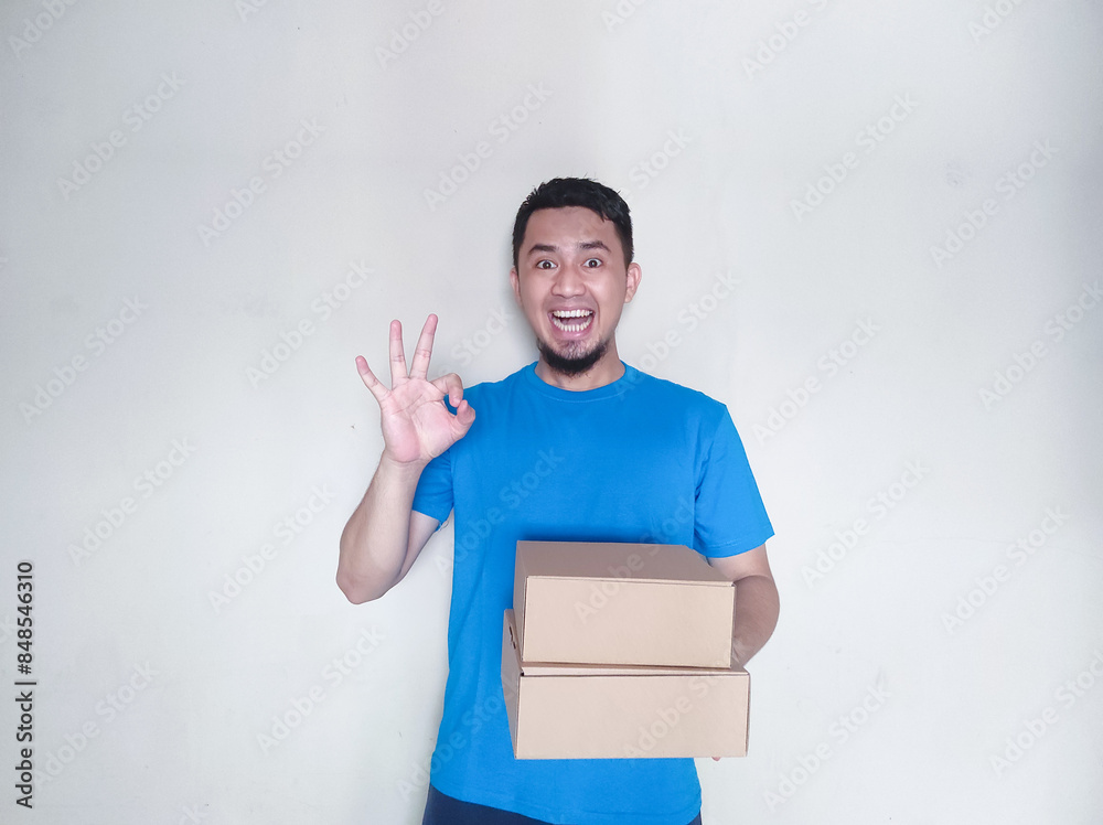 Excited and confident Asian young man making OK hand gesture while holding stack of cardboard boxes, smiling at camera, isolated on white background Excited and confident Asian young man making OK hand gesture while holding stack of cardboard boxes, smiling at camera, isolated on white background