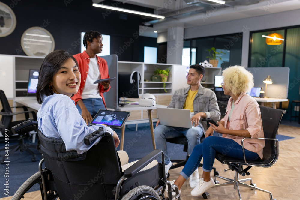 Diverse Business colleagues in office meeting; woman in wheelchair with tablet; startup effort Diverse Business colleagues in office meeting; woman in wheelchair with tablet; startup effort