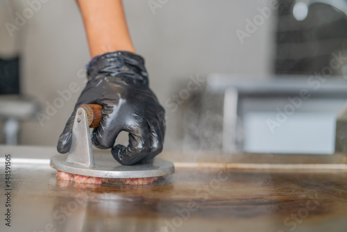 Making smash burgers on the restaurant griddle by smashing them with a utensil