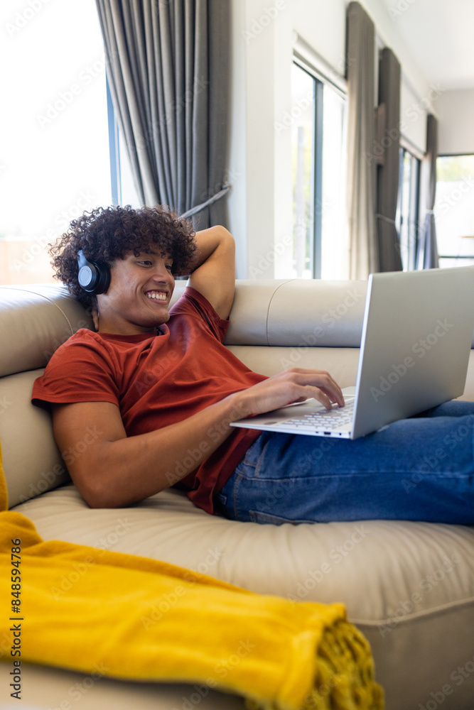 Happy biracial man relaxing on couch with laptop and headphones Happy biracial man relaxing on couch with laptop and headphones
