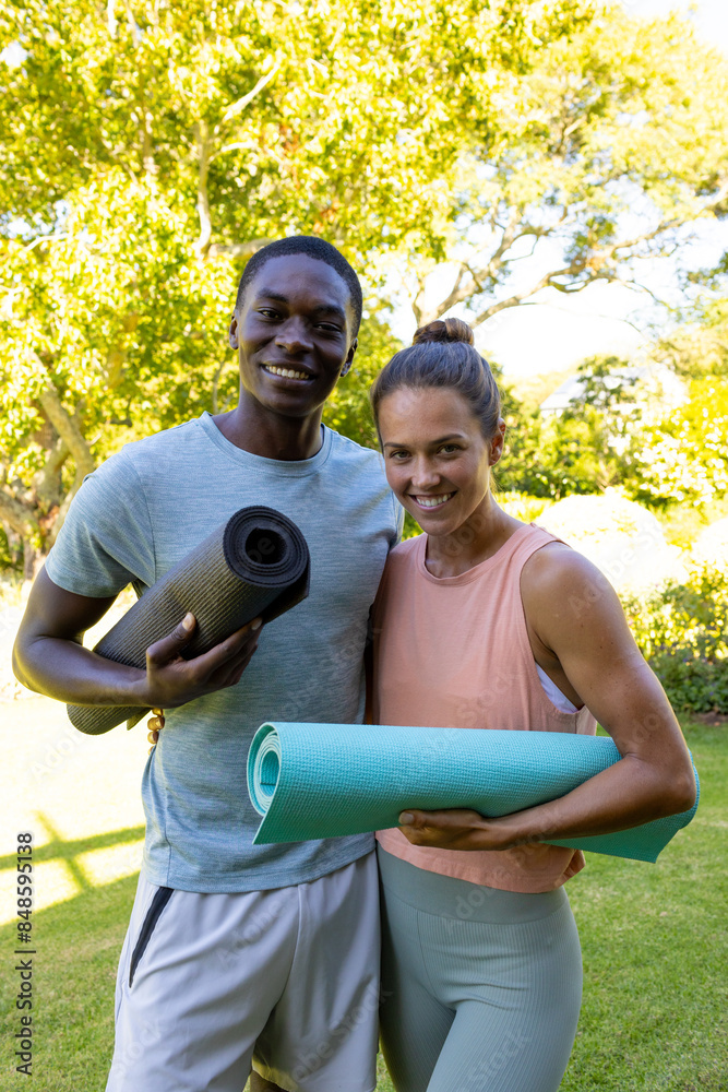 Fit diverse couple in garden, smiling with yoga mats, wellness, healthy lifestyle Fit diverse couple in garden, smiling with yoga mats, wellness, healthy lifestyle