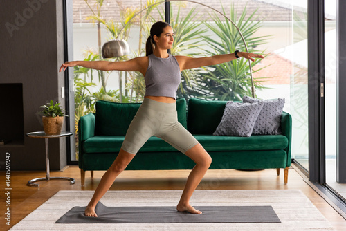Young Caucasian woman practicing yoga in living room, looking fit and relaxed