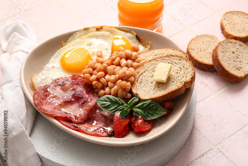 Plate of tasty English breakfast with fried eggs on pink tile background