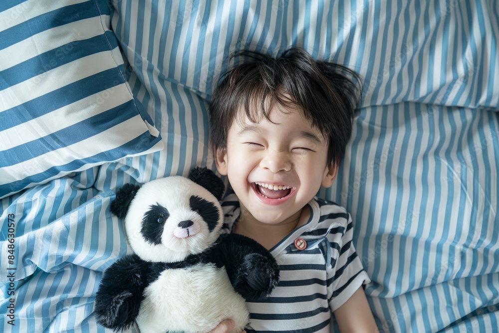 In the top view, an Asian child is lying on the bed, playing with a panda plush toy and smiling happily In the top view, an Asian child is lying on the bed, playing with a panda plush toy and smiling happily