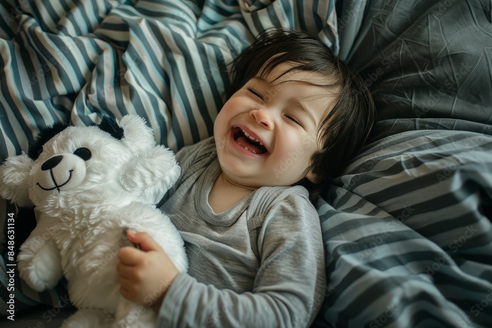 In the top view, an Asian child is lying on the bed, playing with a panda plush toy and smiling happily In the top view, an Asian child is lying on the bed, playing with a panda plush toy and smiling happily