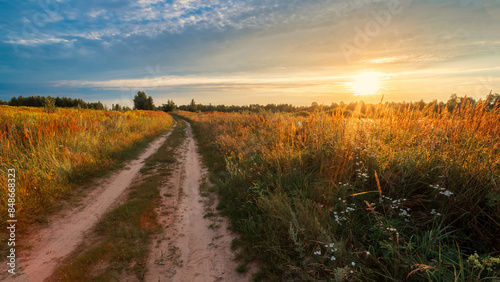 Rural road in a field against the backdrop of a summer sunset.