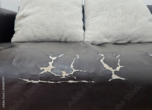 well worn black leather sofa with visible cracks and peeling, two grey cushions rest on the sofa