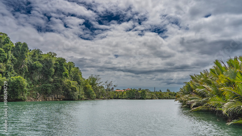 A calm tropical river. The riverbed bends. Ripples on the turquoise water. Thickets of palm trees and lush green vegetation on the banks.  Clouds in the blue sky. Philippines. Bohol. Loboc River    photo