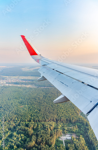 View of airplane wing, blue skies and green land during landing. Airplane window view.