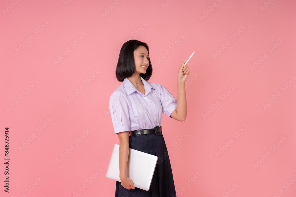 Asian female high school student with short hair Holding a laptop for research and a pen to sign some presentations. Smiling and turning sideways Photographed in a studio with a pink background. Asian female high school student with short hair Holding a laptop for research and a pen to sign some presentations. Smiling and turning sideways Photographed in a studio with a pink background.