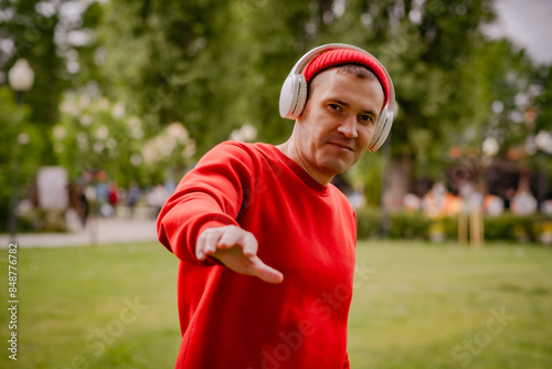 A Man In A Red Sweater Dances With Headphones On In A Park