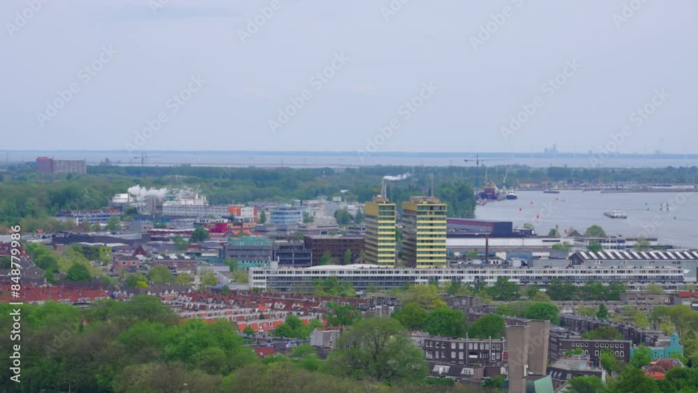 Western aerial view of north Amsterdam, with lush greenery, residential and industrial buildings, and Markermeer lake in the distance, on a cloudy spring day Western aerial view of north Amsterdam, with lush greenery, residential and industrial buildings, and Markermeer lake in the distance, on a cloudy spring day