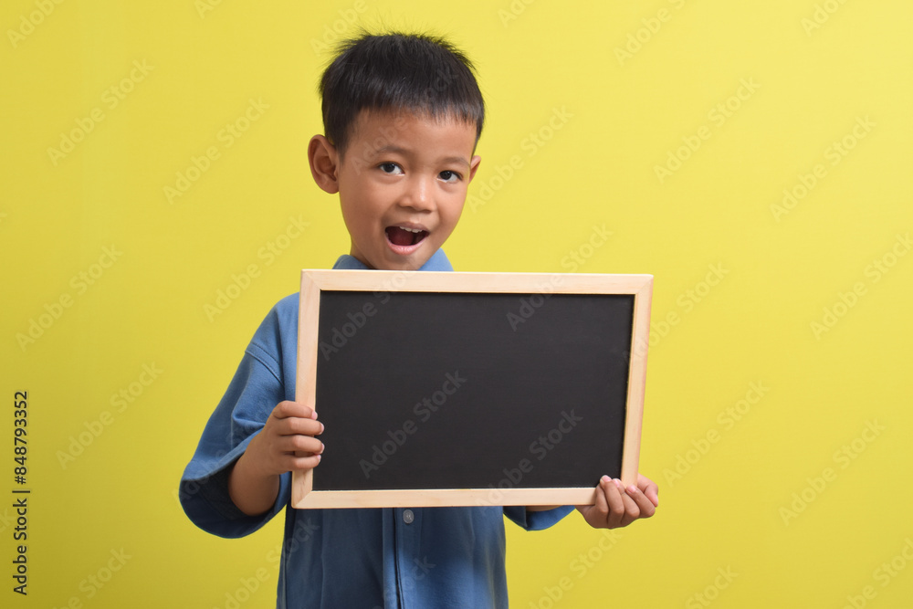 Cute little Asian boy holding a blank chalk board isolated on yellow background. Space for text, copy space, mockup banner Cute little Asian boy holding a blank chalk board isolated on yellow background. Space for text, copy space, mockup banner