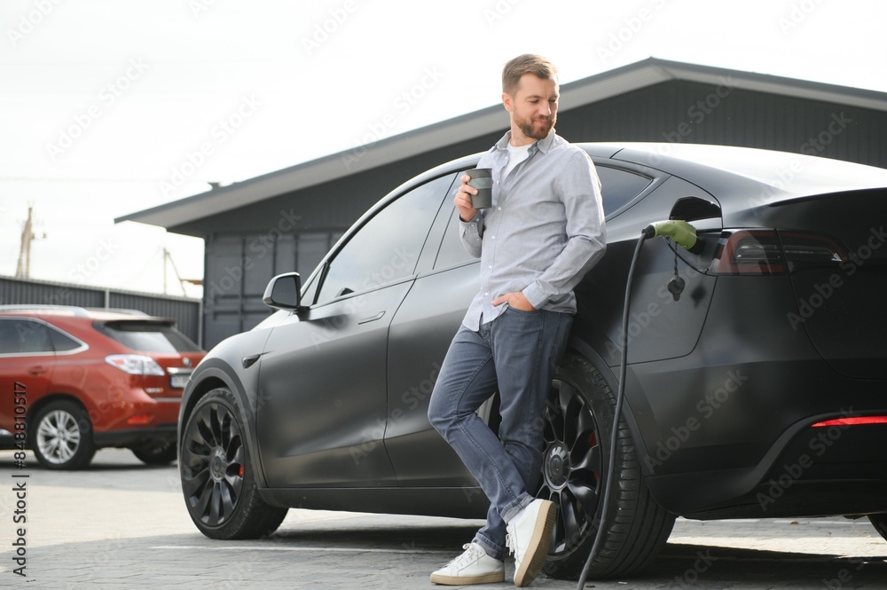 Handsome man drinking coffee while charging electric car Handsome man drinking coffee while charging electric car