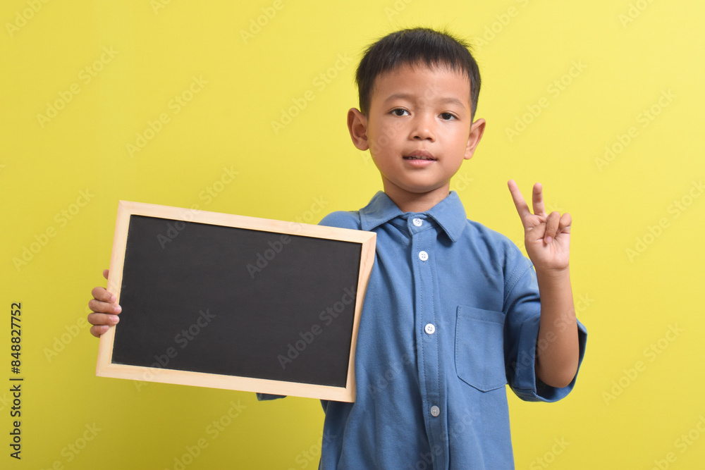 Cute little Asian boy holding a blank chalk board isolated on yellow background. Space for text, copy space, mockup banner Cute little Asian boy holding a blank chalk board isolated on yellow background. Space for text, copy space, mockup banner