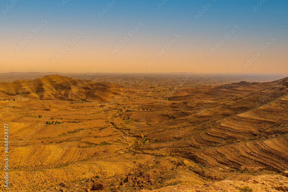 Naklejka premium Magnificent mountainous landscape of the Medenine region of Tunisia. Stunning sunrise over a dry, arid, ochre-coloured mountain range.
