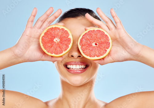 Woman, grapefruit and eyes in studio for skincare, organic and natural cosmetics with vitamin c or citrus acid. Girl, hands and fruit on blue background for hyperpigmentation, detox and healthy glow.