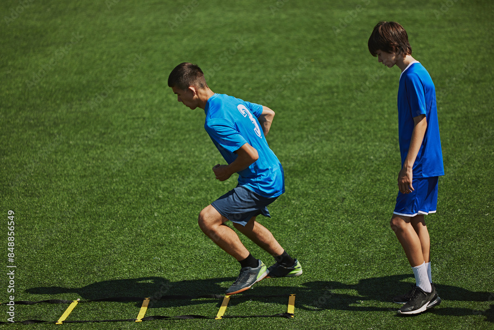 Obraz premium Agility Drill in Action. Two boys in blue jerseys concentrating on agility ladder drill, training, improving quickness and coordination. Concept of sport, school, childhood, hobby, active lifestyle