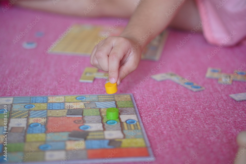 Obraz premium 小学生の子供がボードゲーム遊びを楽しんでいる様子。駒を動かしている手元。