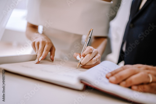 Photography Valmiera, Latvia - September 9, 2023 - Bride signing the wedding register during the ceremony, showcasing a close-up of her hands with a pen and detailed manicured nails