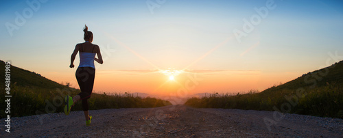 woman running on a mountain road at summer sunset	banner size photo