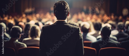 A speaker on stage with a rear view of the audience in a conference hall or seminar embodying business and education concepts all set against a copy space image photo