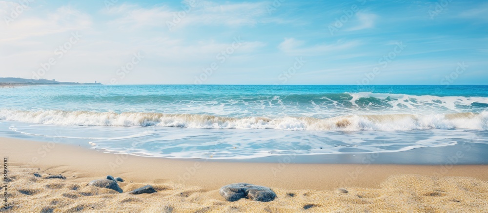 Obraz premium View the horizon from a sandy beach with waves crashing scattered beach stones and a distant land visible across the bay in the copy space image
