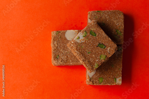 Stacked Homemade Indian mithai (dessert) Besan Gajak Barfi. Made of Til, Desi Ghee, jaggery, and Dry Fruits, on an orange background. Top-down view. Food Flat lay. photo