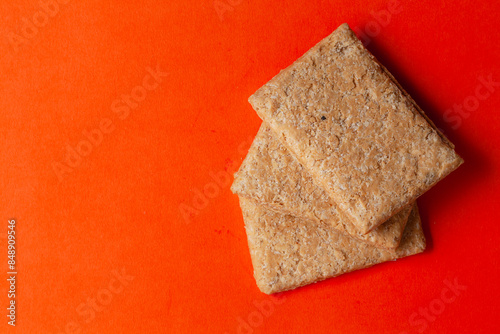 Stacked Indian mithai (dessert), delicate, soft, crunchy Gajak Bars made of Til, Desi Ghee, and Jaggery, on an orange background. Top view. photo