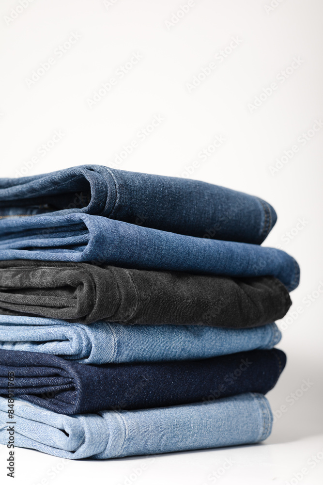 A stack of folded jeans in various shades of blue and black on a white background. A stack of folded jeans in various shades of blue and black on a white background.