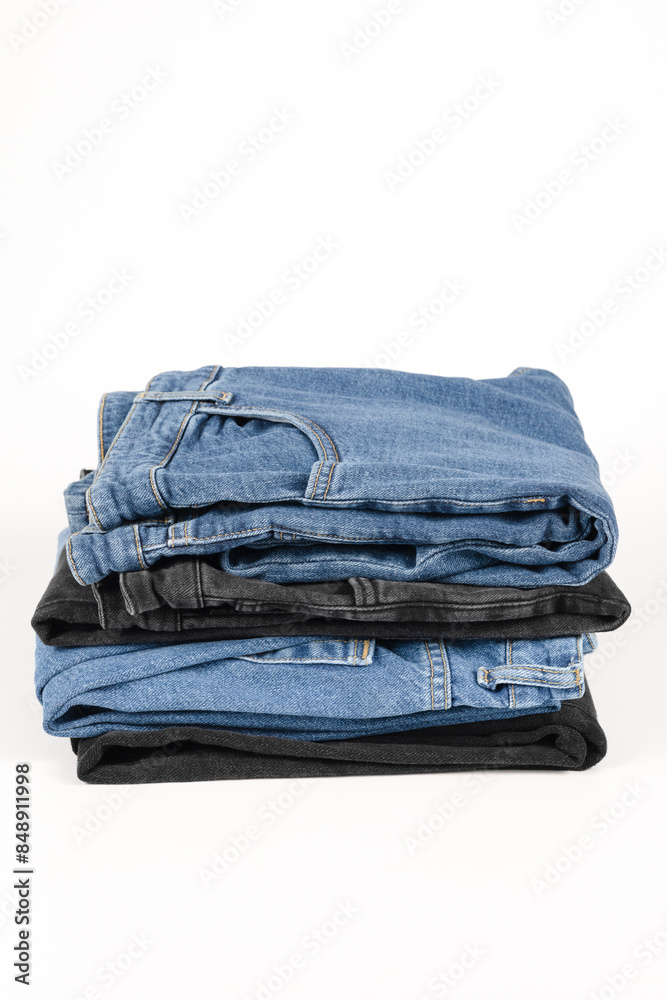 A stack of folded jeans in various shades of blue and black on a white background. A stack of folded jeans in various shades of blue and black on a white background.