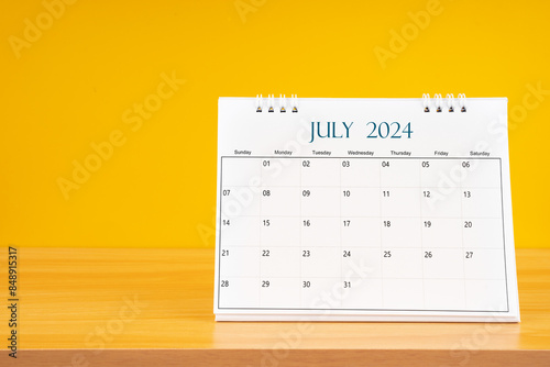 July 2024, Monthly desk calendar for 2024 year on wooden table with yellow background.