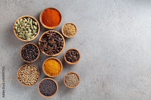 Fototapeta Naklejka Na Ścianę i Meble -  A variety of spices in wooden bowls on a gray background with copyspace top view, vibrant colors and textures.