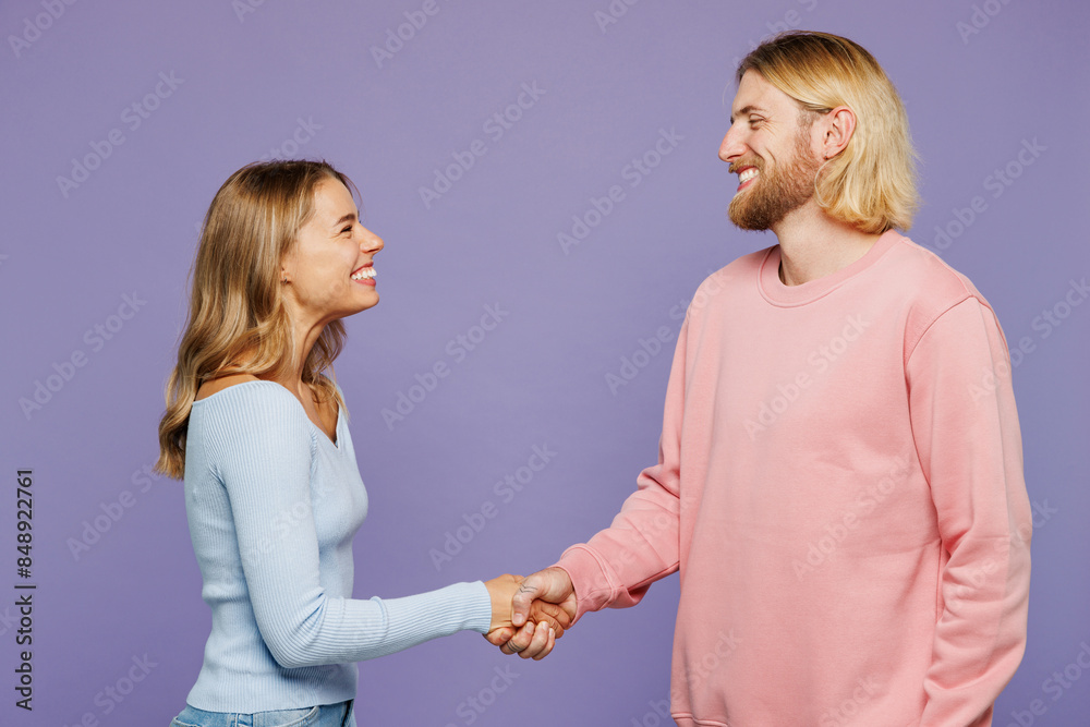 Side profile view smiling fun young couple two friends family man woman wear pink blue casual clothes together do hand shake gesture isolated on pastel plain light purple background studio portrait. Side profile view smiling fun young couple two friends family man woman wear pink blue casual clothes together do hand shake gesture isolated on pastel plain light purple background studio portrait.