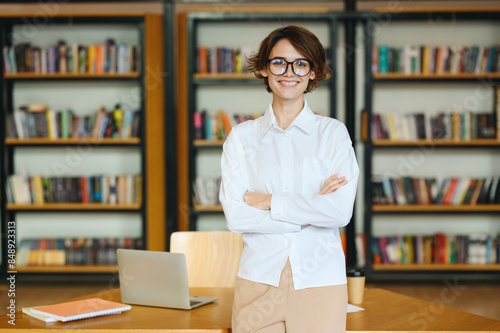 Young fun happy successful employee business woman she wear glasses white shirt casual clothes hold hands crossed folded stand near table work at office desk with pc laptop Achievement career concept photo