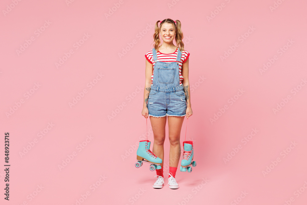 Full body young smiling happy fun woman wear red t-shirt denim overalls casual clothes hold in hand blue rollers look camera isolated on plain pink background. Summer sport lifestyle leisure concept. Full body young smiling happy fun woman wear red t-shirt denim overalls casual clothes hold in hand blue rollers look camera isolated on plain pink background. Summer sport lifestyle leisure concept.