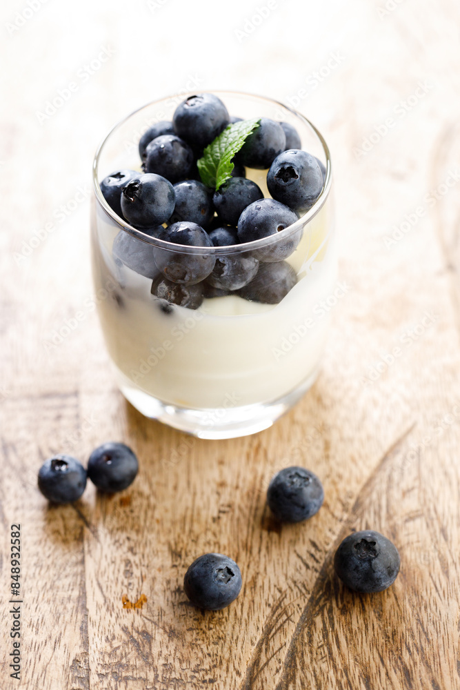 Ripe organic blueberries with yogurt in a glass on rustic wooden table background. Selective focus. Ripe organic blueberries with yogurt in a glass on rustic wooden table background. Selective focus.