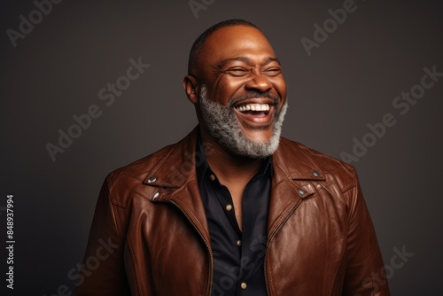 Portrait of a cheerful afro-american man in his 50s sporting a stylish leather blazer on minimalist or empty room background