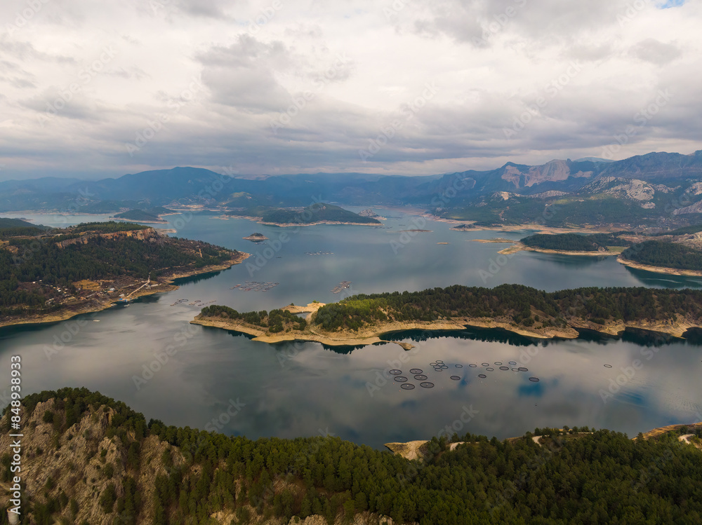 A dam lake in Turkey surrounded by forests. Fish cages in the lake. Cloudy sky. Karacaoren dam, Bucak, Burdur, Turkey. A dam lake in Turkey surrounded by forests. Fish cages in the lake. Cloudy sky. Karacaoren dam, Bucak, Burdur, Turkey.