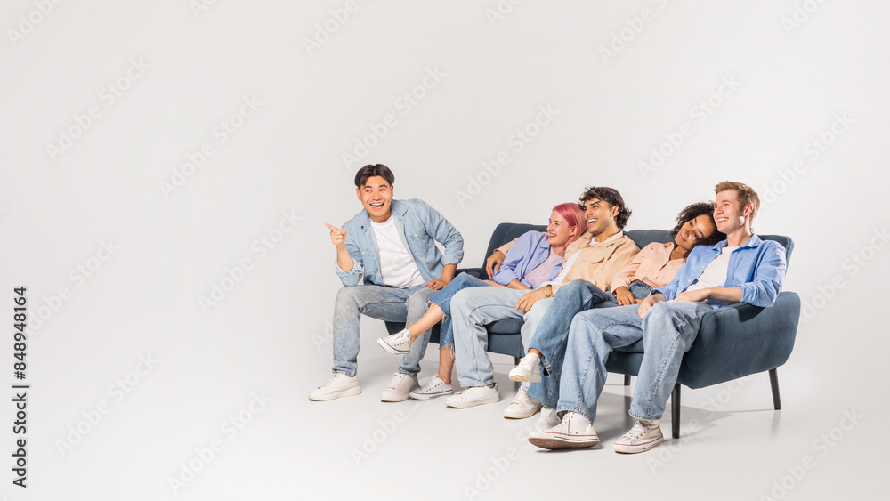 A group of five friends are enjoying each others company, laughing and smiling. The diverse group of young adults are casually dressed in denim and sitting on a couch in a light studio space. A group of five friends are enjoying each others company, laughing and smiling. The diverse group of young adults are casually dressed in denim and sitting on a couch in a light studio space.