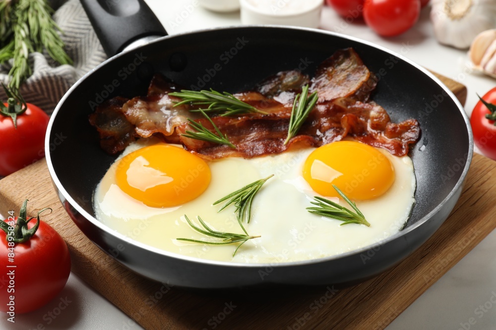 Tasty bacon, eggs and rosemary in frying pan on light table, closeup Tasty bacon, eggs and rosemary in frying pan on light table, closeup